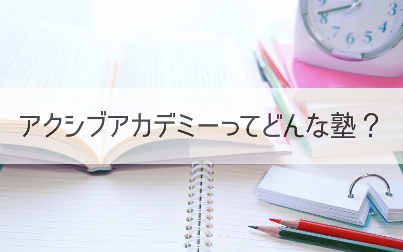 テキストとノートとペン、時計と「アクシブアカデミーってどん な塾?」の文字