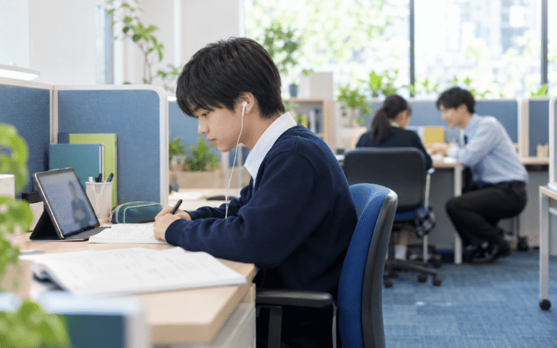 タブレットで学習する中学生と、別の生徒をやさしく指導する先生がいる個別指導塾の教室